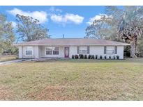 Ranch style home with red front door, well-manicured lawn and mature trees at 5724 Se 2Nd St, Ocala, FL 34480