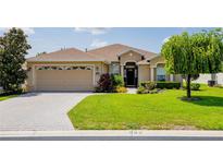 Tan one-story house with a two-car garage, landscaped yard, and brick paver driveway at 15890 Sw 11Th Terrace Rd, Ocala, FL 34473