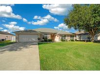 Tan house with a two-car garage and American flag at 9890 Sw 55Th Ct, Ocala, FL 34476