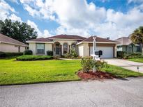 Single-story house with a brown tile roof, a well-manicured lawn, and a paved driveway at 6688 Sw 113Th Pl, Ocala, FL 34476