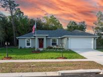 Gray one-story house with a red door, two-car garage, and landscaped lawn at 7735 Sw 148Th St, Ocala, FL 34473