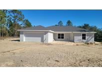 Front exterior view of a single-story home with a gray facade, attached garage, and partially finished driveway at 5083 Sw Hyacinth Ct, Dunnellon, FL 34431