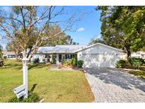 White house with gray roof, landscaped yard, and brick paver driveway at 10195 Se 178Th Pl, Summerfield, FL 34491