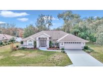 Single-story home with a light-brown facade, two-car garage, and landscaped lawn at 5370 Sw 85Th Ln, Ocala, FL 34476