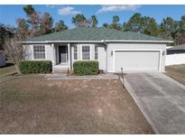 One-story house featuring a green roof, attached garage, and manicured landscaping at 8457 Sw 138Th Pl, Ocala, FL 34473