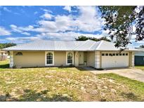 Tan one-story home with metal roof, white garage door, and manicured lawn at 814 Cambridge Way, Lake Wales, FL 33853