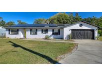 White brick ranch house with solar panels, attached garage, and landscaped lawn at 1610 Meadow Ne Ln, Winter Haven, FL 33881