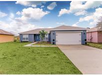 Newly built home with a blue exterior, white garage door, and well-manicured lawn at 1414 Hillsborough Dr, Poinciana, FL 34759