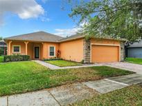 Orange house exterior with a two-car garage and landscaping at 153 Marabella Loop, Poinciana, FL 34759