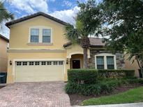 Two-story house with a yellow facade, brick driveway, and lush landscaping at 2131 Tripoli Ct, Kissimmee, FL 34747