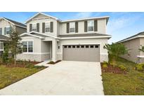 Two-story home with neutral siding, a stone facade, and a two car garage at 180 Flag Lilly Ln, Umatilla, FL 32784