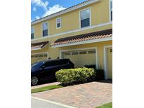 Two-story townhome with yellow exterior, two-car garage, and brick pavers at 14434 Swanley St, Orlando, FL 32832