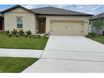 Tan one-story house with a two-car garage and well-manicured lawn at 833 Orchid Grove Blvd, Davenport, FL 33837