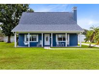 Charming blue house with a white porch, rocking chairs, and a spacious lawn at 435 Lantern Dr, Kenansville, FL 34739
