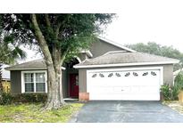 One-story house with a gray exterior, lush landscaping and a white garage door at 2556 Bear Creek Ct, Kissimmee, FL 34747