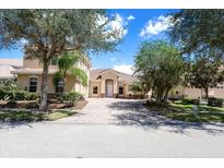 Two-story house with tan exterior, paver driveway, and lush landscaping at 3757 Eagle Isle Cir, Kissimmee, FL 34746