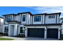 Two-story house with a modern design, featuring a white facade, dark gray garage doors, and black window frames at 1427 Butterfly Milkweed, Davenport, FL 33837