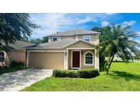 Two-story house with tan exterior, red door, two-car garage, and landscaped lawn at 2668 Whispering Trails Dr, Winter Haven, FL 33884