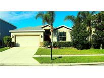 Tan house with a white garage door, landscaping, and palm trees at 1569 Thetford Cir, Orlando, FL 32824