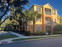 Condo building exterior, featuring a yellow and orange facade, palm trees, and ample parking at 6265 Contessa Dr # 203, Orlando, FL 32829