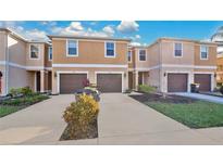 Tan three-story townhouses with brown garages, landscaping, and a paved driveway at 1336 Chelsea Dr, Davenport, FL 33897