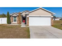 Tan house with red door, white garage door, and landscaping at 825 Desmoines Pl, Kissimmee, FL 34759