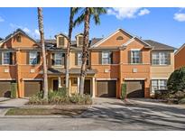 Orange townhouses with brown garages, palm trees, and lush landscaping at 879 Assembly Ct, Reunion, FL 34747