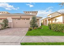 Tan two-car garage home with brick paver driveway and landscaping at 2482 Yellow Brick Rd, St Cloud, FL 34772