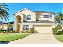Two-story house with beige exterior, two-car garage, and manicured lawn at 1020 Golf Course Pkwy, Davenport, FL 33837