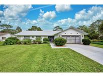 Single story home with attached garage, manicured lawn, and mature landscaping at 7491 Limonia Dr, Indian Lake Estates, FL 33855