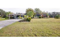 Ranch style home with carport, mature landscaping, and spacious lawn at 6085 Amaryllis Dr, Indian Lake Estates, FL 33855