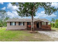 Tan one-story house with a wooden porch and large tree in the front at 1230 8Th Ave, Deland, FL 32724