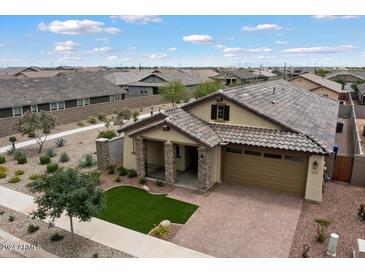 Aerial view of a tan house with a brick driveway and green lawn at 16143 W Charlotte Dr, Surprise, AZ 85387