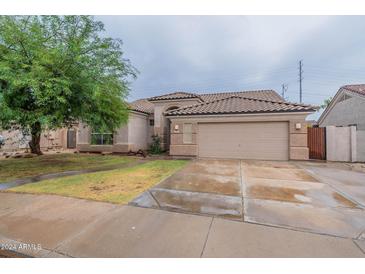 Tan one-story house with a tile roof, two-car garage, and a tree in front at 7951 E Posada Ave, Mesa, AZ 85212