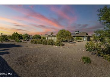 Spacious backyard with gravel landscaping and mature trees under a sunset sky at 12442 W Marble Dr, Sun City West, AZ 85375