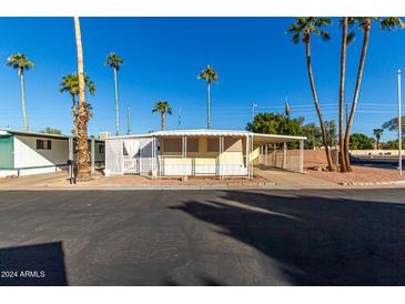 Tan mobile home with covered porch and white lattice fence, surrounded by palm trees at 4065 E University Dr # 01, Mesa, AZ 85205