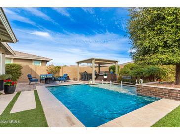 Inviting backyard oasis featuring a sparkling pool, covered patio, and lush landscaping at 2949 N Acacia Way, Buckeye, AZ 85396