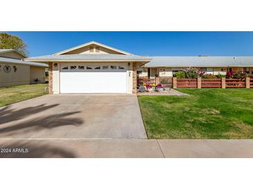 House exterior featuring a white garage door, well-manicured lawn, and a brick walkway at 10728 W Cheryl Dr, Sun City, AZ 85351