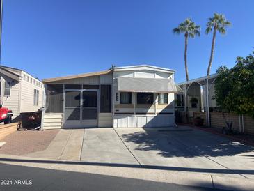 Tan mobile home with screened porch and paved driveway, situated in a sunny location at 1437 S Zuni Dr, Apache Junction, AZ 85119