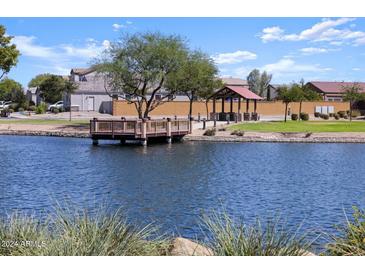 Scenic community lake with a wooden pier, gazebo, and lush green grass at 36943 W Prado St, Maricopa, AZ 85138