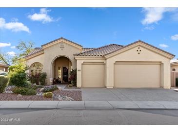 Beige stucco home with arched entryway, three-car garage, and desert landscaping at 1613 W Ainsworth Dr, Anthem, AZ 85086