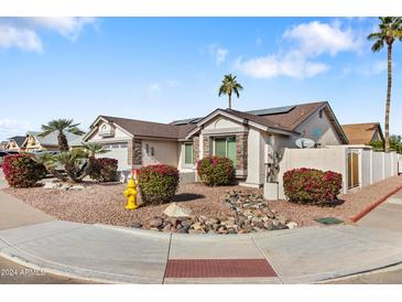 Single-story home with desert landscaping, stone accents, and a solar panel system at 7744 W Midway Ave, Glendale, AZ 85303