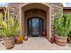 Inviting entryway with ornate iron door, stone facade, and mature cacti in large pots at 35140 N 52Nd Pl, Cave Creek, AZ 85331