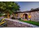 Stone exterior with arched entryway, landscaping, and lighting at 10719 E Rimrock Dr, Scottsdale, AZ 85255