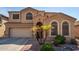 Two-story house with tan exterior, arched windows, three palm trees, and a two-car garage at 16079 W Williams St, Goodyear, AZ 85338