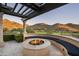 Round fire pit with built-in seating under a pergola, overlooking mountains at 10493 E Rimrock Dr, Scottsdale, AZ 85255