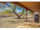 Covered patio with tile flooring, overlooking a gravel backyard with mature trees at 2125 W Bromm Ln, Wickenburg, AZ 85390