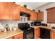 Clean kitchen with wood cabinets, black appliances, and a large sink at 45759 W Morning View Ln, Maricopa, AZ 85139