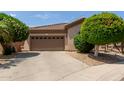 Exterior view of a beige house with a brown garage door and well-manicured landscaping at 2074 E Hulet Pl, Chandler, AZ 85225