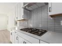 Modern kitchen with white cabinets, gas cooktop, and gray tile backsplash at 17637 W Blue Sky Dr, Surprise, AZ 85387